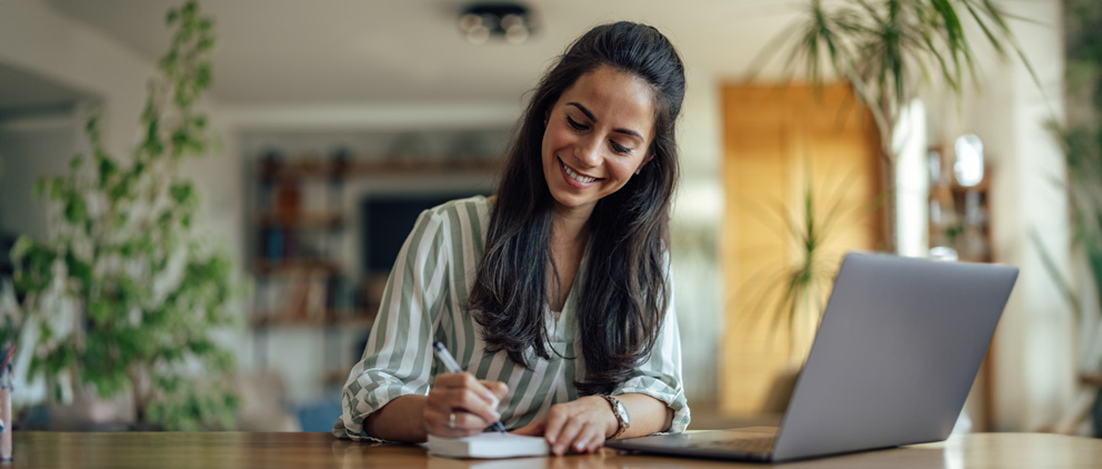 Smiling woman at a table writing in a check registry