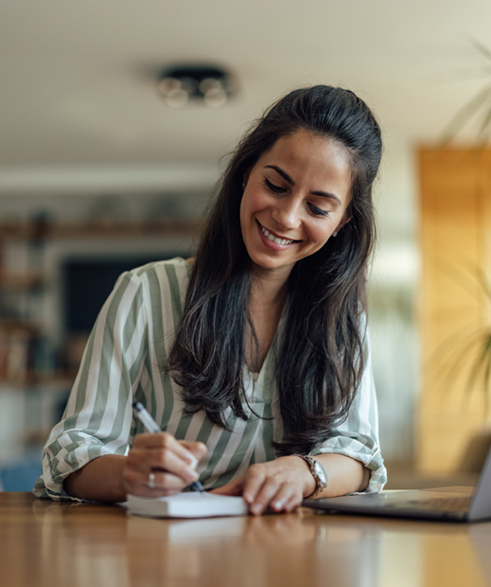 Smiling woman at a table writing in a check registry