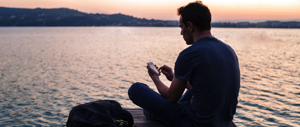 Man sitting on the end of a dock using his ServU mobile banking app