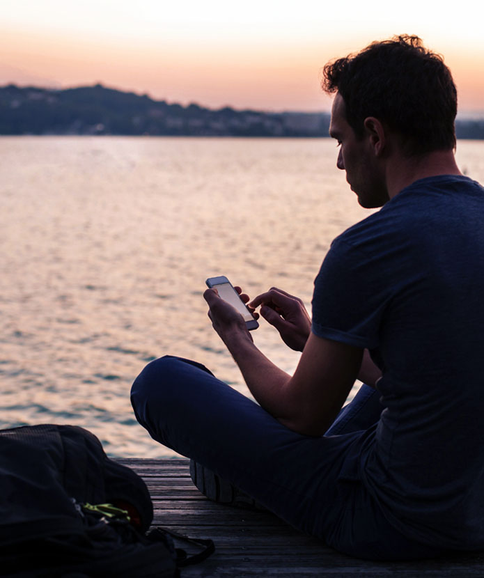 Man sitting on the end of a dock using his ServU mobile banking app