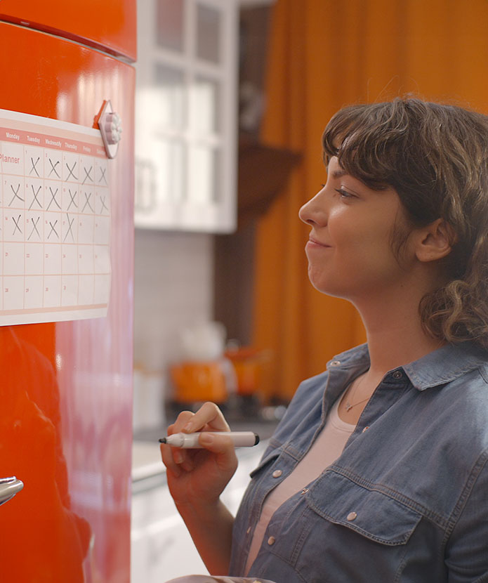 Someone updating a calendar she has posted on her refrigerator door