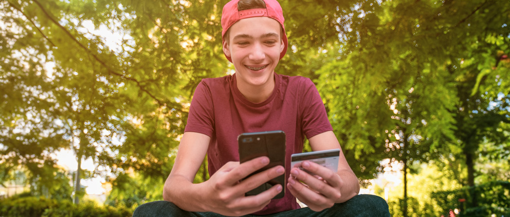 Teen boy smiling while using his mobile phone and credit card