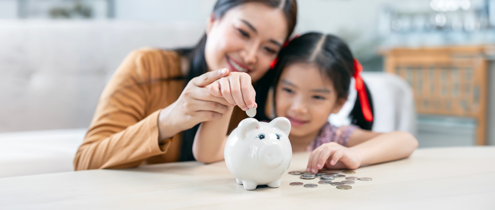 A mom showing her daughter how to save money for the future by putting coins in a piggy bank