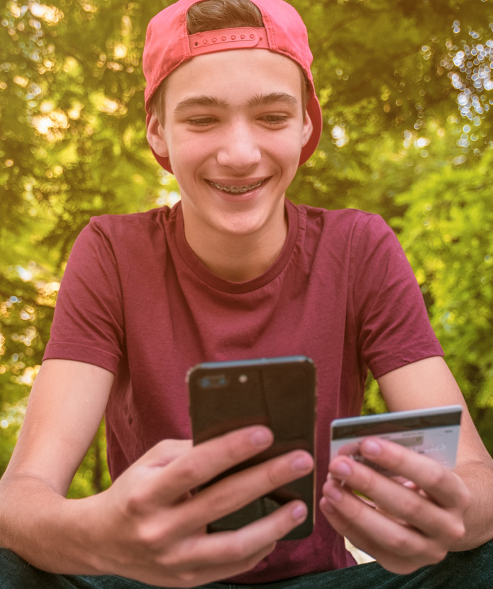 Teen boy smiling while using his mobile phone and credit card