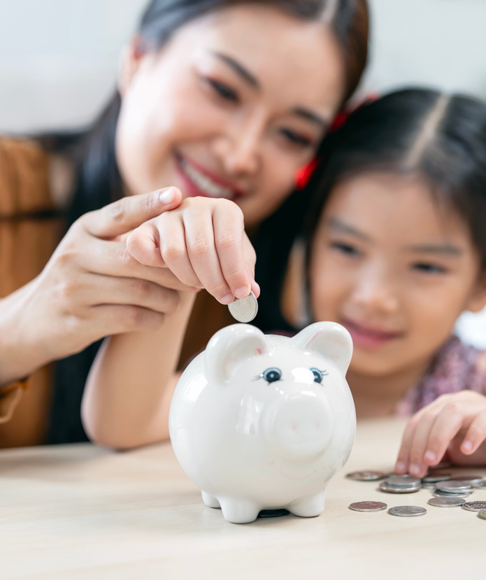 A mom showing her daughter how to save money for the future by putting coins in a piggy bank